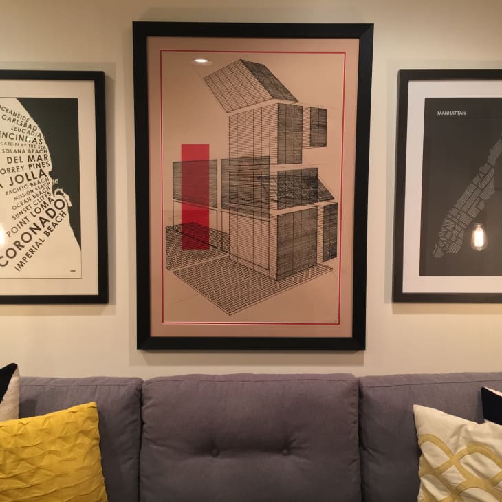 Three framed artworks above a gray sofa with yellow and patterned pillows.