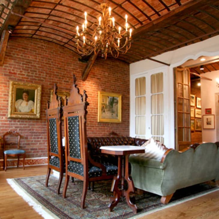 Exposed brick living room with chandelier, vintage furniture, and framed art on walls.