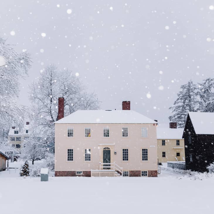 Historic houses in a snowy landscape with falling snowflakes and bare trees.