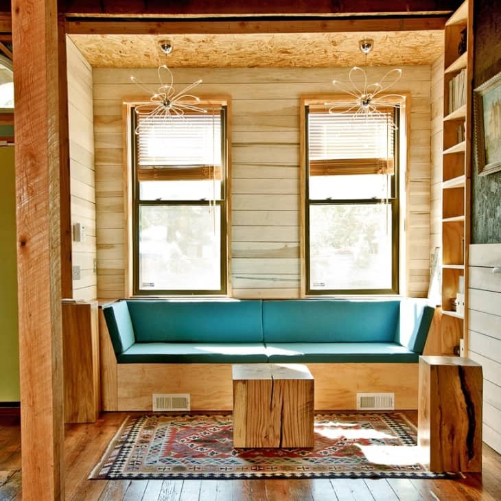 Cozy nook with teal bench seating, wooden accents, two windows, and a patterned rug.