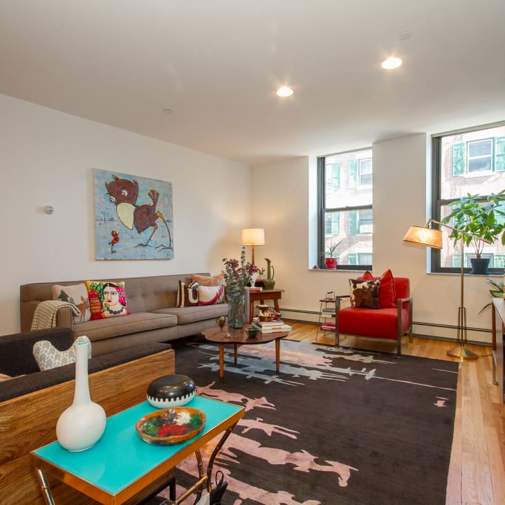 Living room with a gray sectional, red armchair, colorful pillows, abstract art, and large windows.