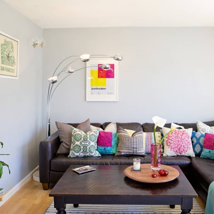 Living room with a dark sectional sofa, colorful pillows, a wooden coffee table, and modern floor lamp.