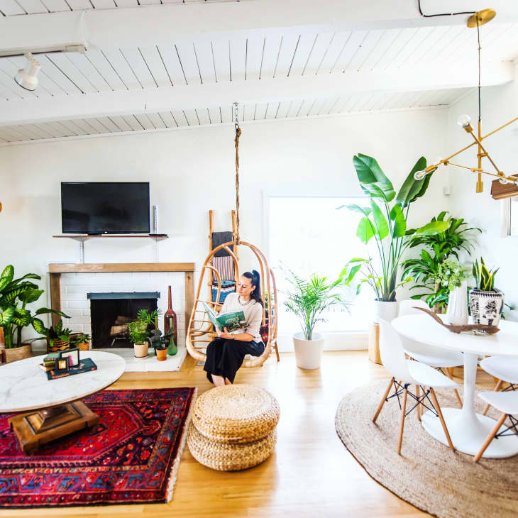 Bright living room with hanging chair, plants, red rug, round dining table, and modern chandelier.