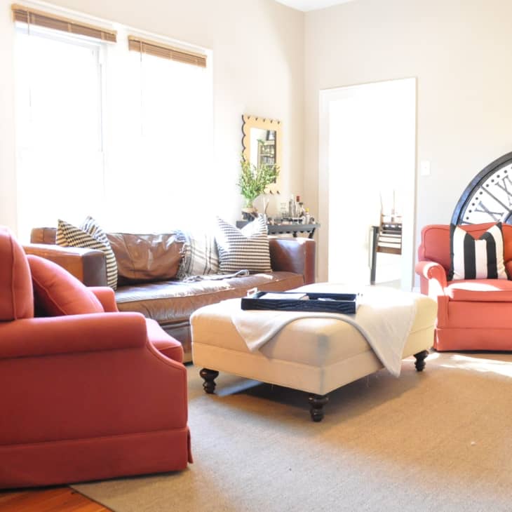 Living room with red armchairs, brown sofa, large clock decor, and beige ottoman on a rug.