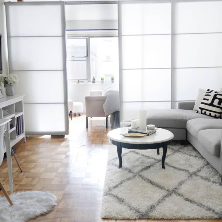 Modern living room with gray sectional sofa, geometric pillows, white shag rug, and round coffee table with candles.