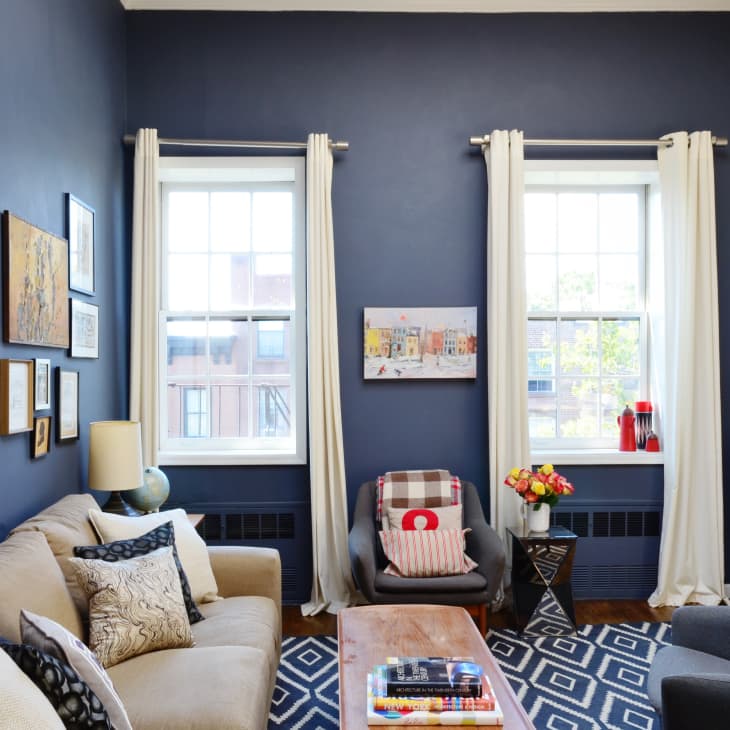 Living room with blue walls, beige sofa, gallery wall, two windows, and a patterned rug.