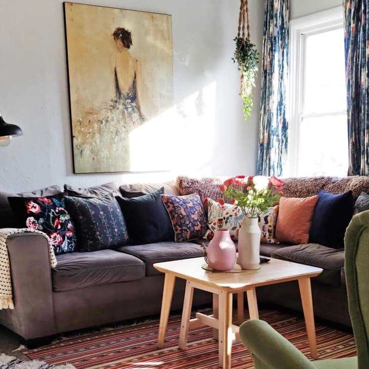 Cozy living room with a gray sectional sofa, colorful pillows, floral artwork, and a wooden coffee table with vases.