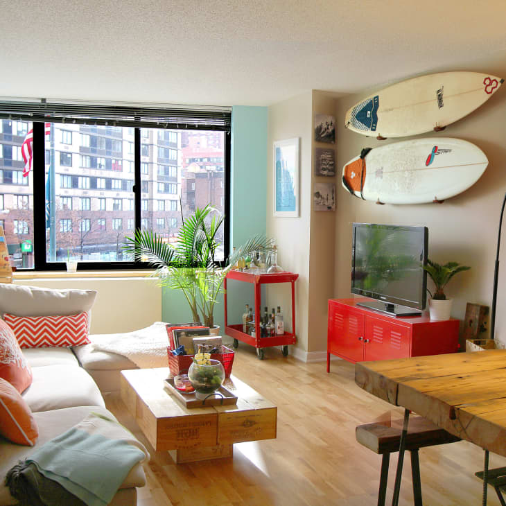 Modern living room with surfboards on wall, red TV stand, large window, beige sectional sofa, and wooden dining table.