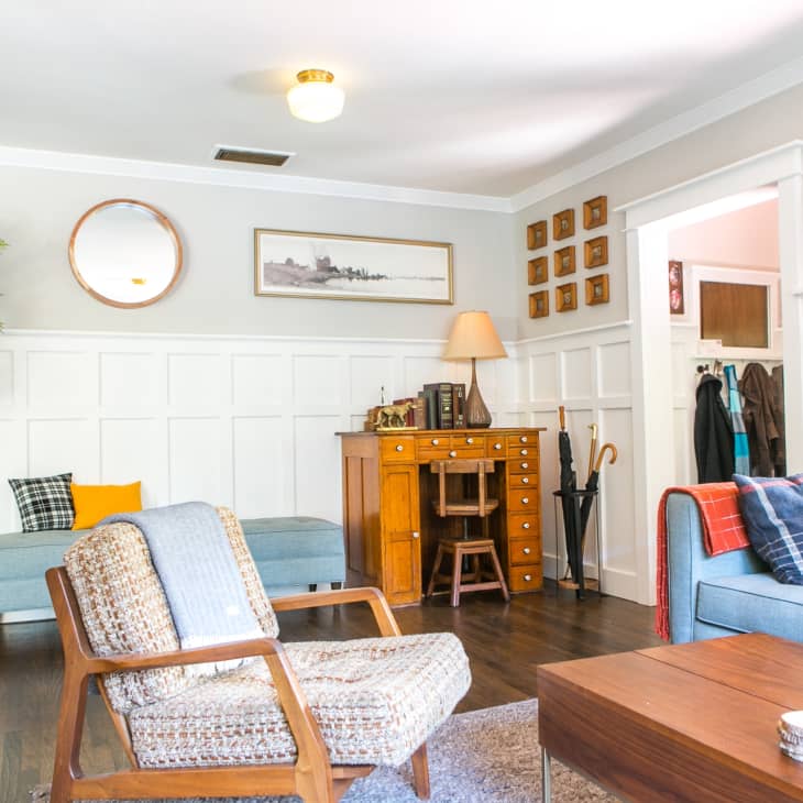 Living room with blue sofa, wooden desk, armchair, wall art, and potted plant, featuring cozy decor and natural light.