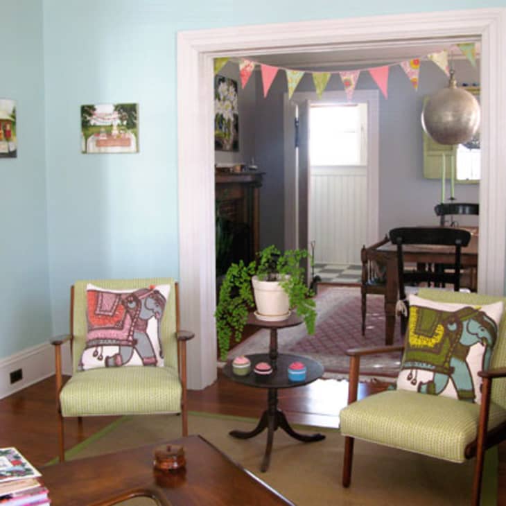 Living room with two armchairs featuring elephant cushions, a small round table with cups, and a doorway with bunting.