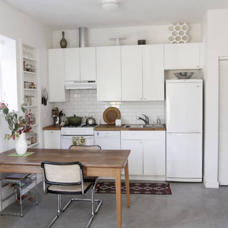 Minimalist kitchen with white cabinets, wooden table, single chair, and decorative vase with flowers.