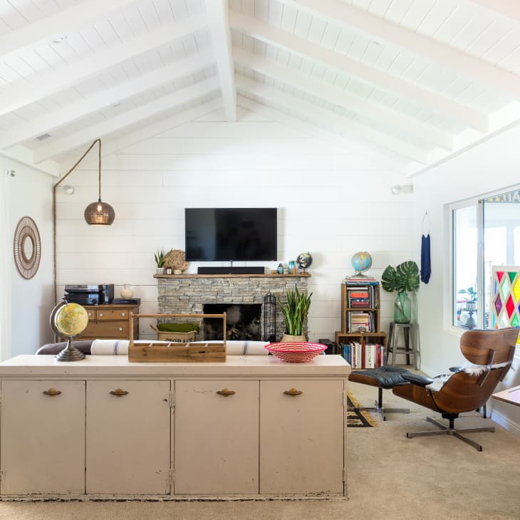 Living room with vaulted ceiling, TV above stone fireplace, globe, bookshelves, leather chair, and colorful stained glass.