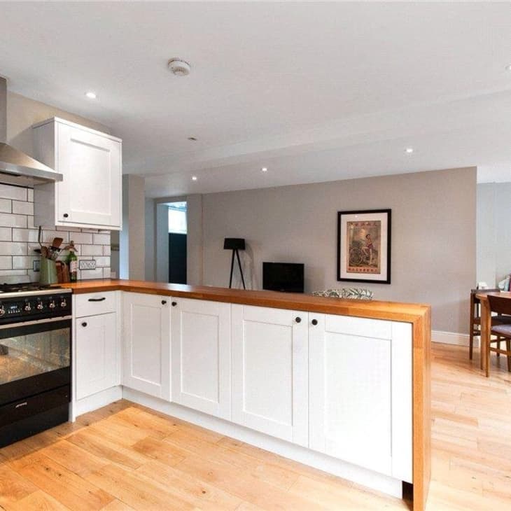 Modern kitchen with white cabinets, wood countertops, black stove, and open dining area with framed art and bookshelves.
