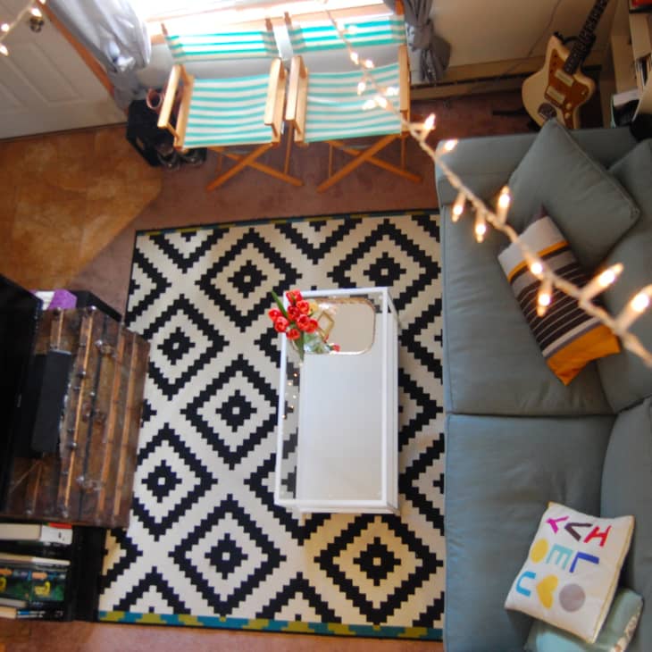 Cozy living room with a blue sofa, geometric rug, white coffee table, and string lights.