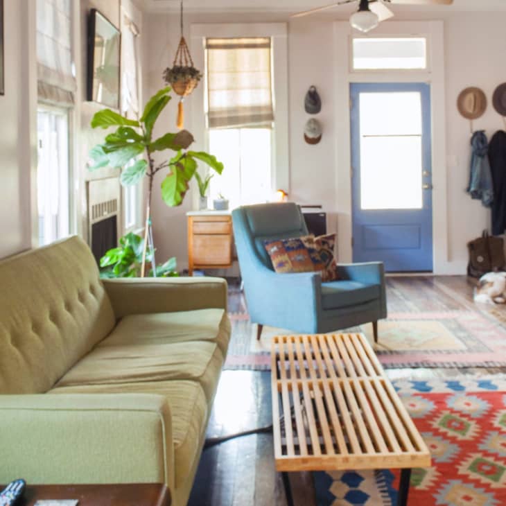 Living room with green sofa, blue armchair, colorful rug, wooden coffee table, and potted plant near a blue door.