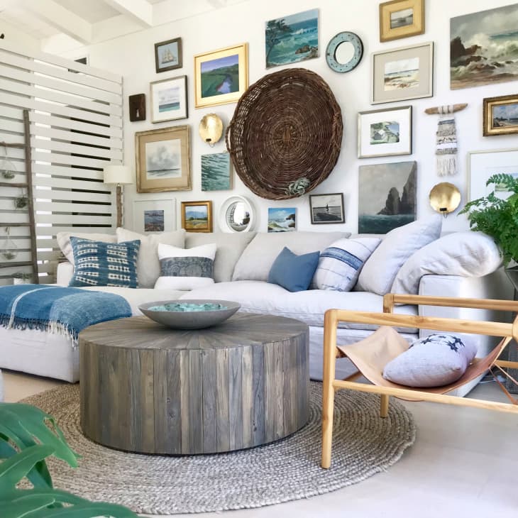 Cozy living room with a white sofa, blue pillows, wooden coffee table, and a gallery wall of coastal-themed artwork.