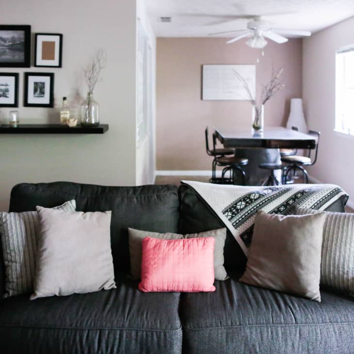 Dark gray sofa with assorted pillows and a patterned throw, facing a dining area with a black table and chairs.