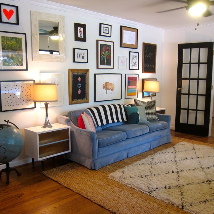 Living room with blue sofa, eclectic gallery wall, globe, and lamps on side tables, featuring a black-framed glass door.