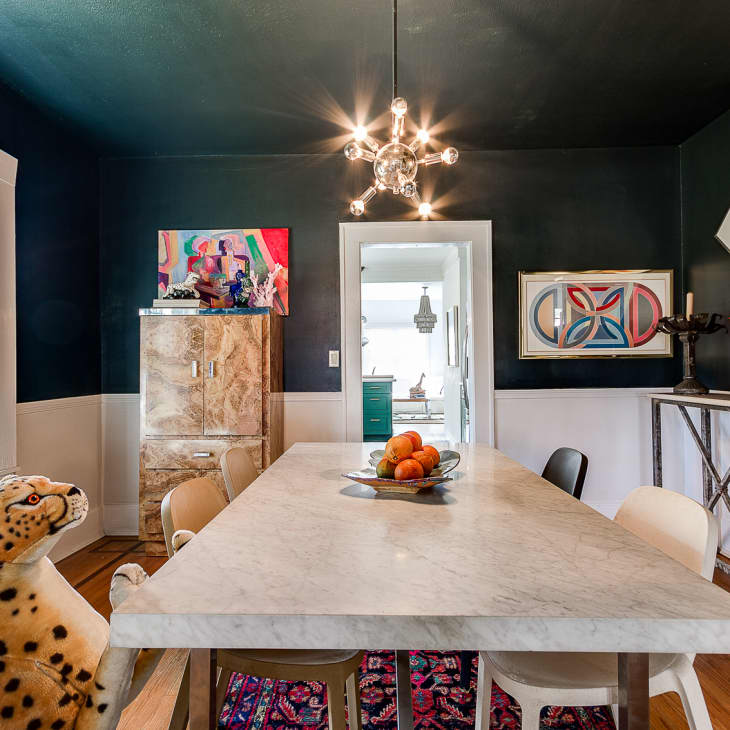 Dining room with marble table, eclectic art, leopard statue, and modern chandelier, featuring a bowl of oranges.