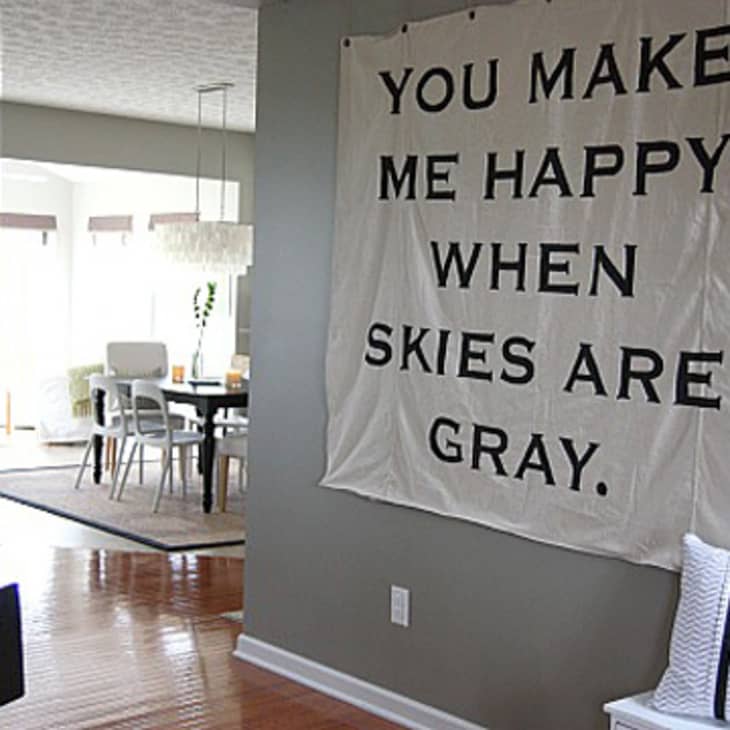 Wall hanging with "You make me happy when skies are gray" in a modern dining room with wooden floors.