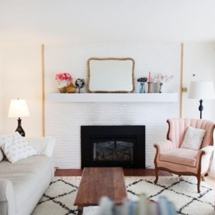 Living room with a beige sofa, pink armchair, white brick fireplace, and a wooden coffee table.