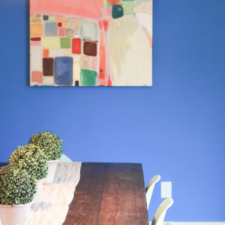 Dining room with blue walls, abstract painting, dark wood table, and potted plants.