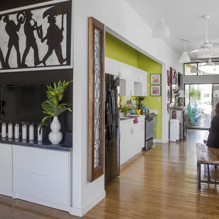 Open-concept kitchen and dining area with green accent wall, plants, and a person working at a wooden table.