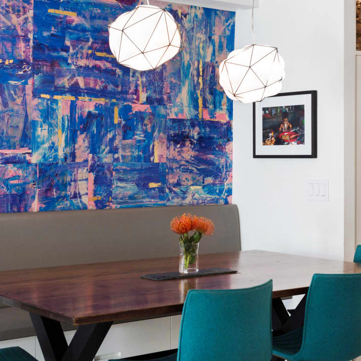 Dining area with a wooden table, teal chairs, abstract blue wall art, and geometric pendant lights.