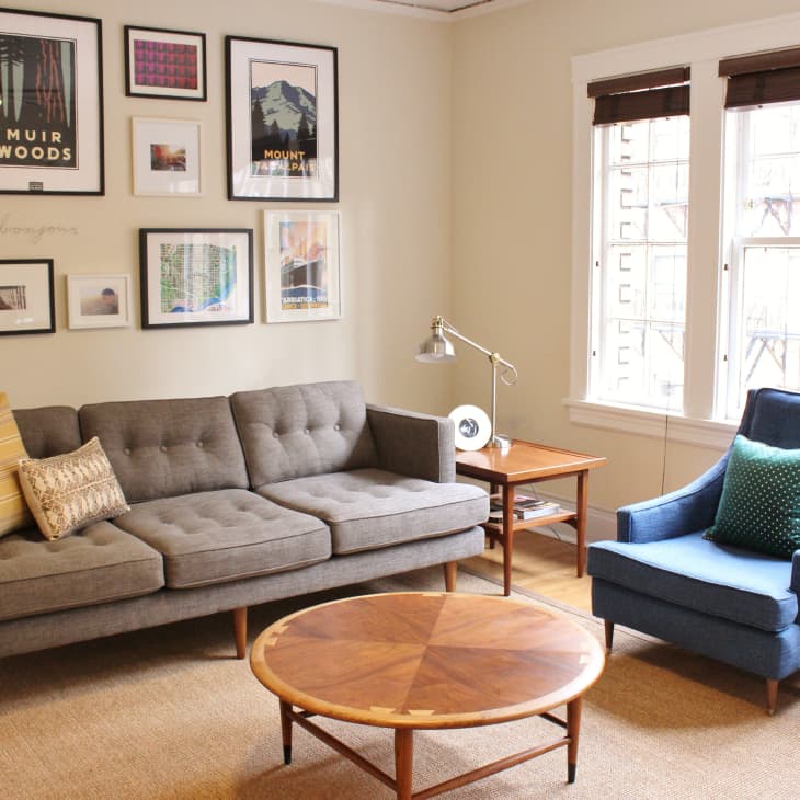 Living room with gray sofa, blue armchair, round wooden table, and framed art on the wall.