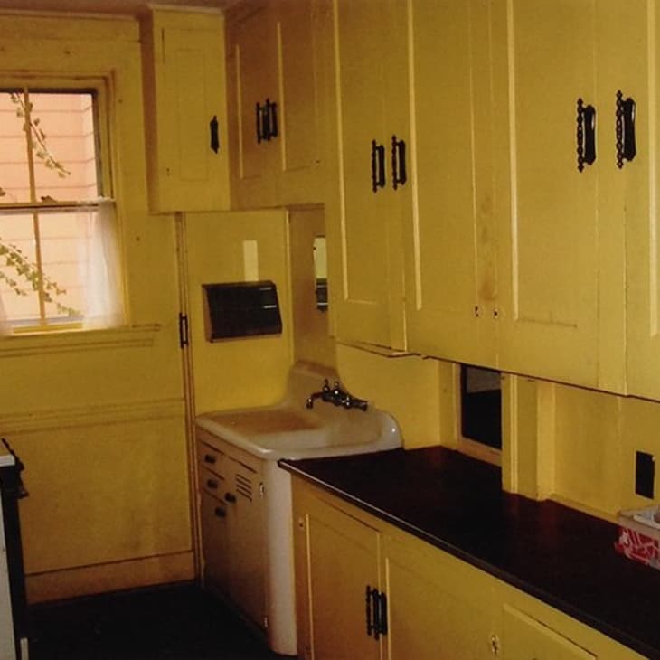 Yellow kitchen with vintage cabinets, dark countertops, a small window, and a stove.