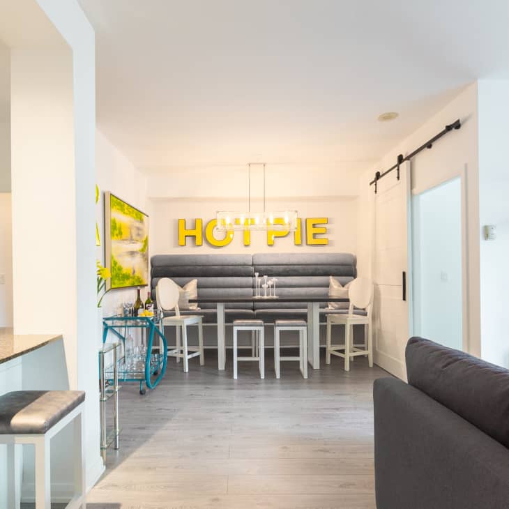 Dining area with gray banquette seating, white chairs, and "HOT PIE" in yellow letters on the wall.