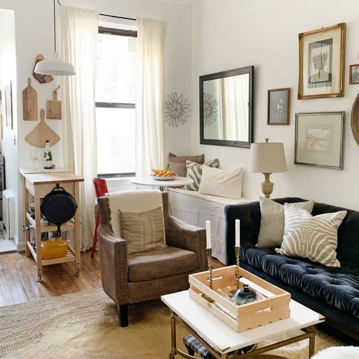 Cozy living room with dark sofa, armchair, wall art, and a view into a small kitchen with wooden accents.