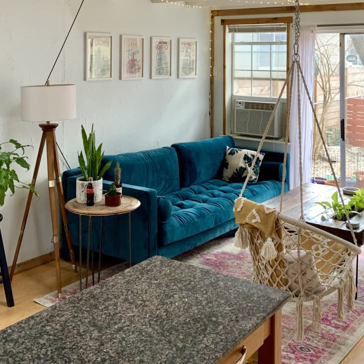 Living room with teal sofa, hanging chair, plants, and a wooden coffee table near sliding glass doors.