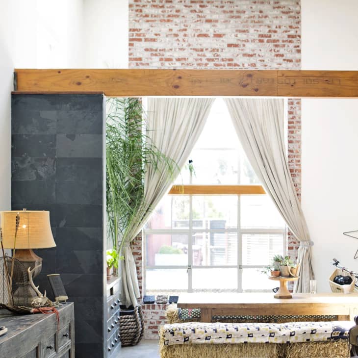 Loft-style living room with exposed brick, large window, wooden beam, and eclectic decor including a star wall art and potted plants.