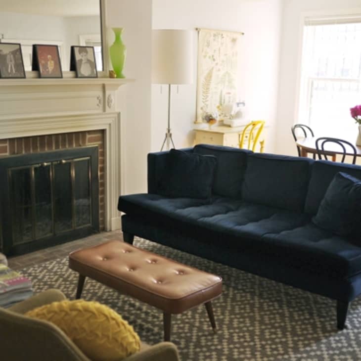 Living room with a navy blue sofa, patterned rug, fireplace, and dining table with pink flowers.