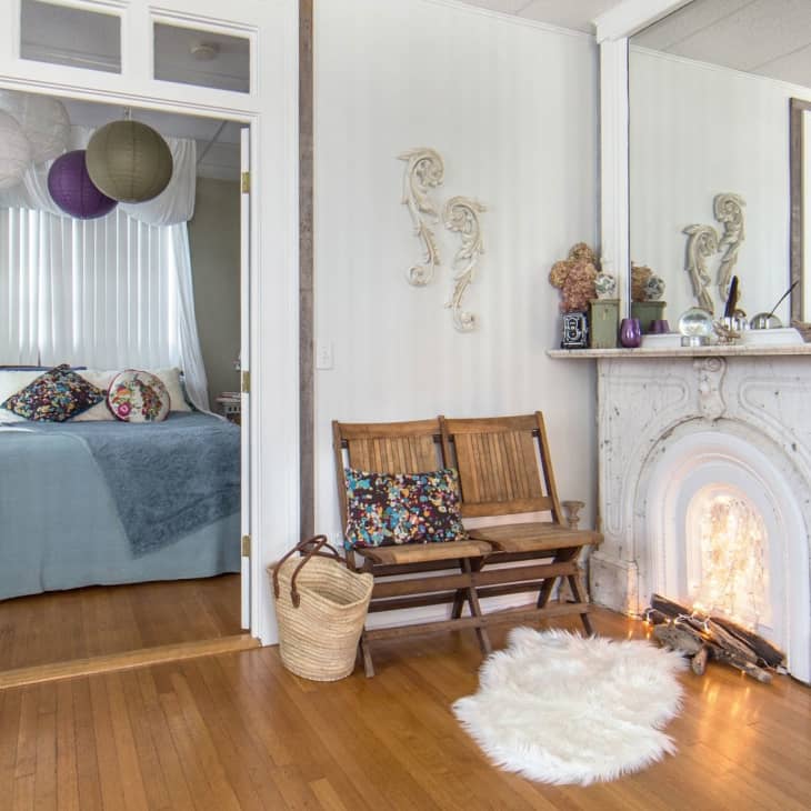 Bedroom with blue bedding, paper lanterns, wooden bench, and ornate white fireplace with decorative items.