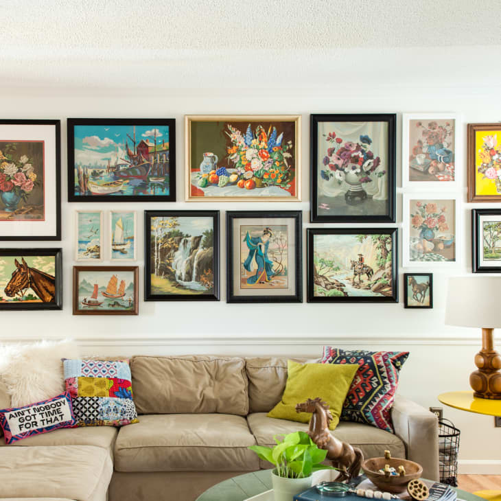 Gallery wall with eclectic framed art above a beige sectional sofa, colorful pillows, and a yellow side table with a lamp.