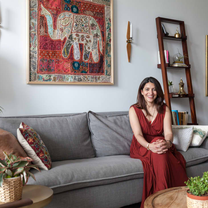 Woman in red dress sitting on gray sofa in living room with elephant tapestry, plants, and wooden ladder shelf.