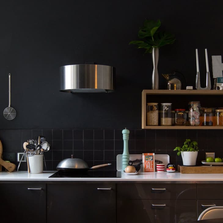 Modern kitchen with dark cabinets, open shelves with jars, a plant, and a stainless steel range hood.