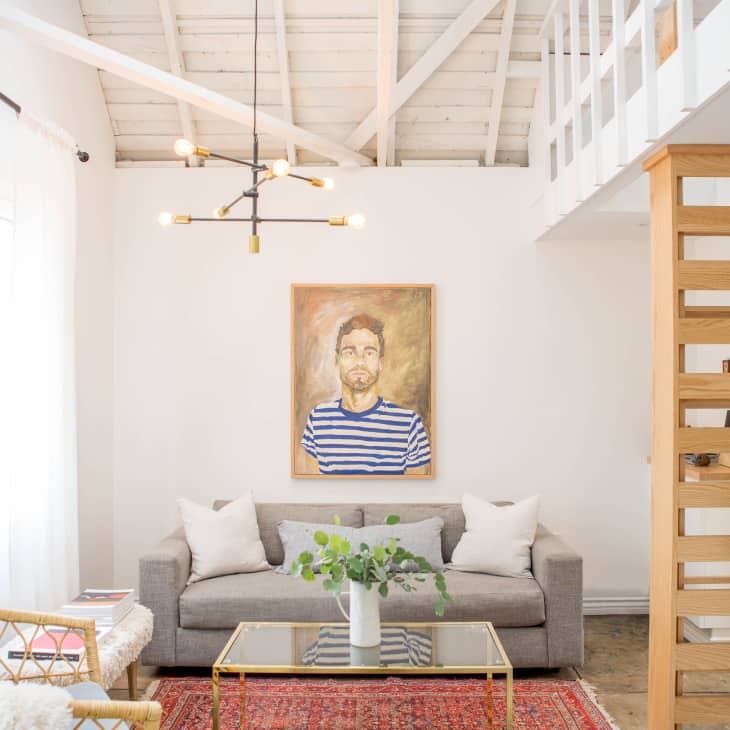 Living room with gray sofa, portrait painting, modern chandelier, red rug, and wooden staircase.
