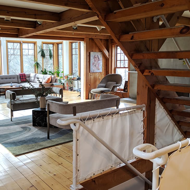 Spacious living room with wooden beams, large windows, gray sofas, and indoor plants.