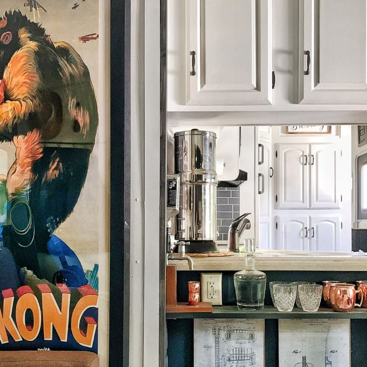 Retro King Kong poster beside a kitchen counter with copper mugs, glassware, and a water filter.