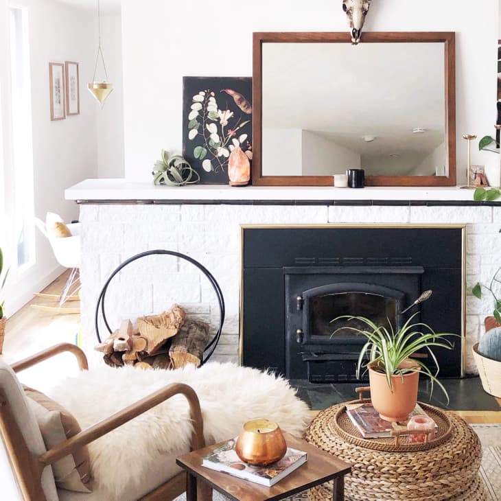 Cozy living room with a white fireplace, plants, wicker basket, and a mirror above the mantel.