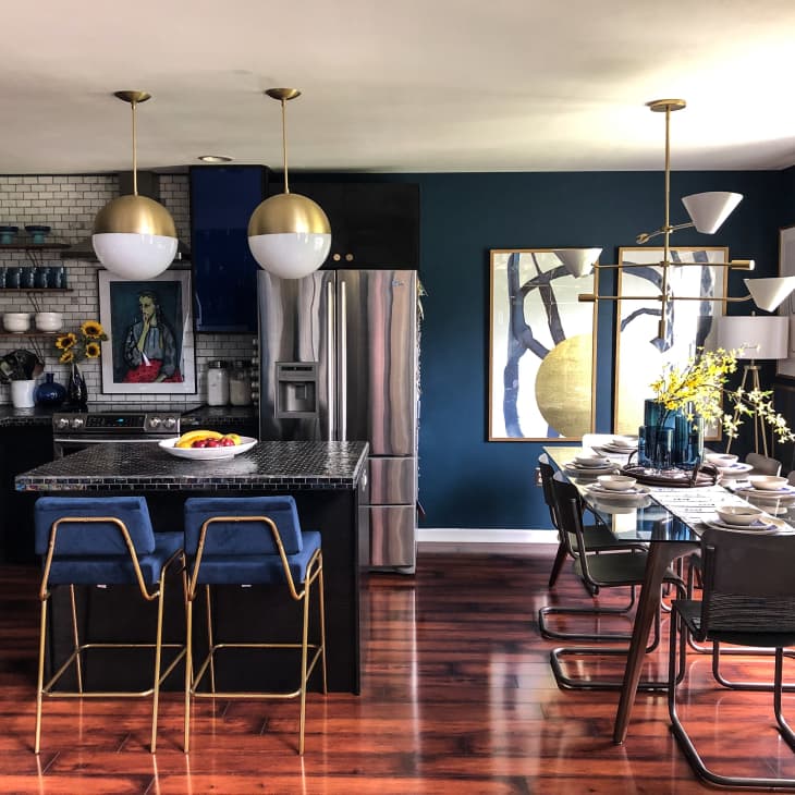Modern kitchen and dining area with dark cabinets, blue bar stools, gold pendant lights, and a set dining table with floral decor.