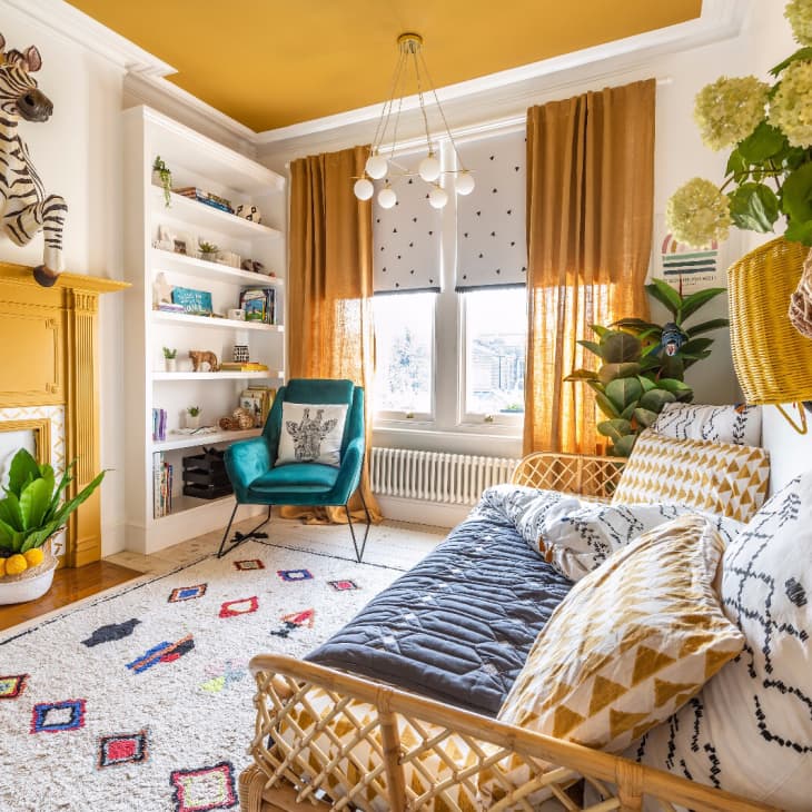Eclectic living room with yellow fireplace, zebra sculpture, teal chair, patterned rug, and hanging plants.