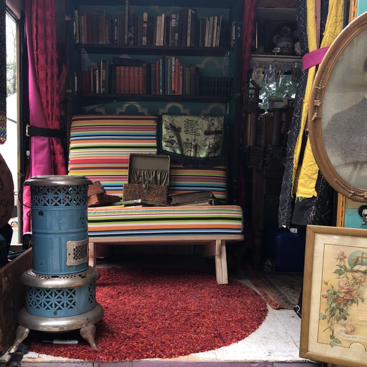 Eclectic room with striped chair, blue stove, red rug, bookshelves, and vintage portraits.