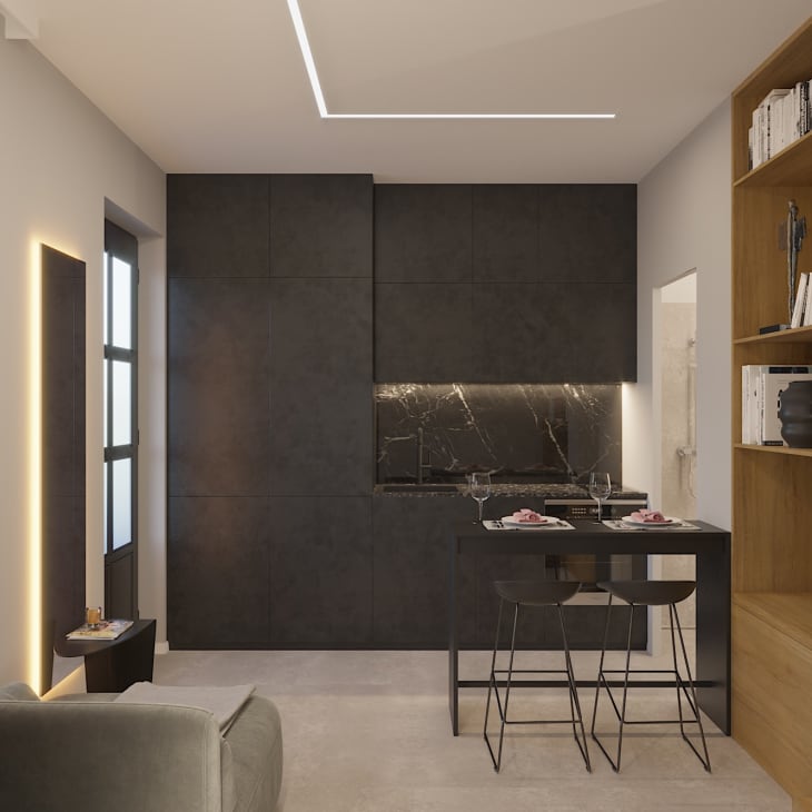 Modern kitchen with black cabinets, marble backsplash, small dining table with two stools, and wooden bookshelf.