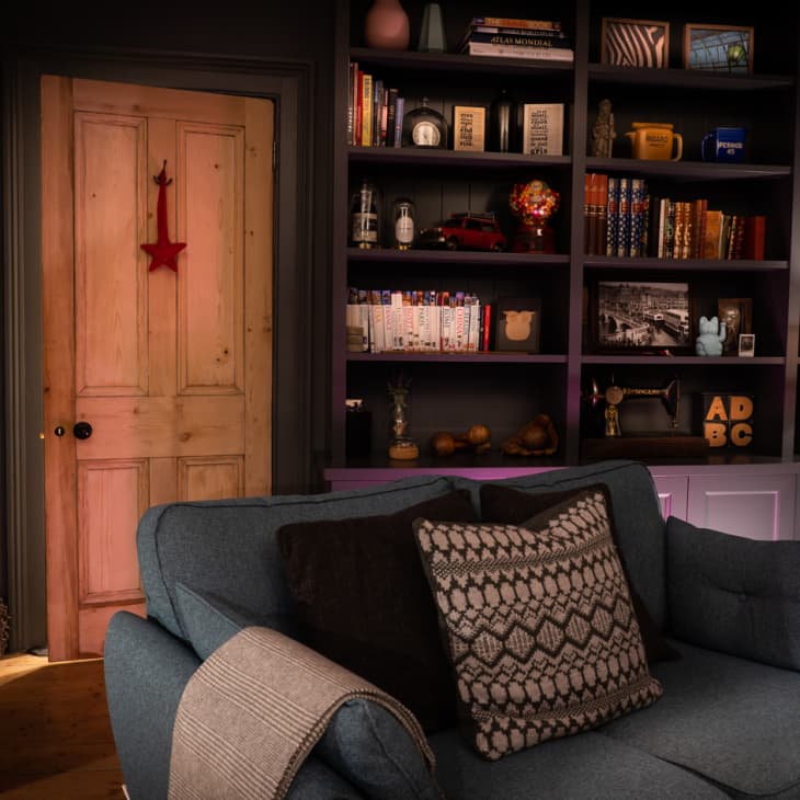 Cozy living room with a blue sofa, patterned pillow, wooden door, and bookshelves filled with books and decor items.