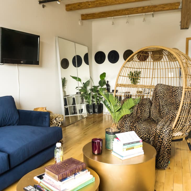Living room with blue sofa, rattan egg chair, leopard print cushion, wall-mounted TV, and mirrored closet doors.