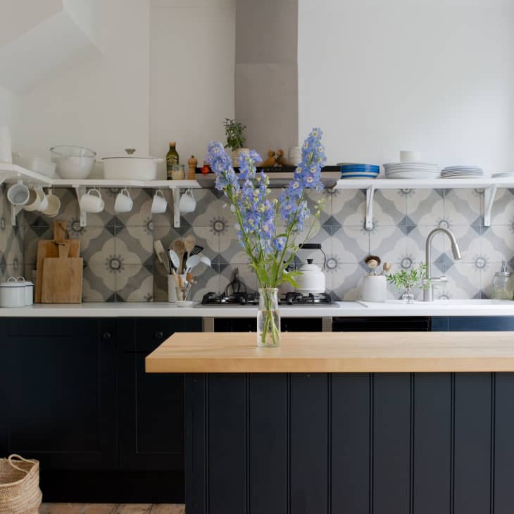 Modern kitchen with black cabinets, patterned backsplash, open shelves, and a vase of blue flowers on a wooden island.